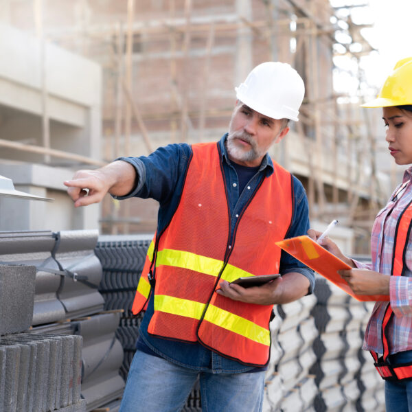 senior civil engineer inspects the bricks and roof tile at real estate project with his secretary, supplier delivers at site. Elder Engineer and Junior wearing reflective jacket and helmet for safety.
